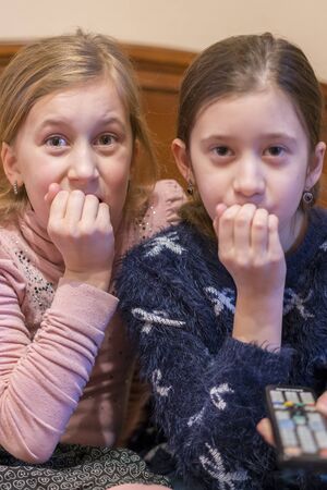 people, children, television, friends and friendship concept - two scared little girls watching horror on tv at home. Vertical photo. toned.の写真素材