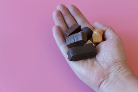 Hand with chocolates on a pink background. Enjoying sweets. Sweet addiction concept. The concept of...