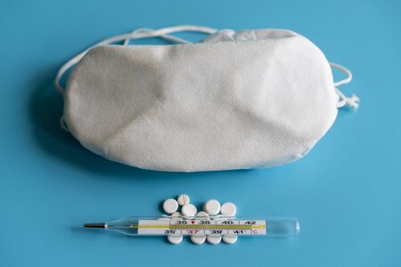 thermometer, pills and a protective mask on a blue background. Virus protection and treatment...