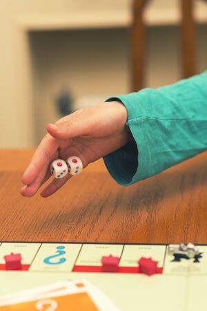A girl playing a board game and rolls dice. Hand throws the dice on the background of colorful blurred fantasy Board games, gaming moments in dynamics. toned.の写真素材