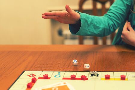 A girl playing a board game and rolls dice. Hand throws the dice on the background of colorful blurred fantasy Board games, gaming moments in dynamics. toned.の写真素材