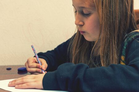 Schoolgirl draws at a desk. Little girl student studying sitting at her desk. School, education, knowledge and children. tonedの写真素材