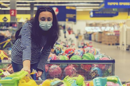 Woman in a protective mask in a supermarket chooses children's toys. toned.