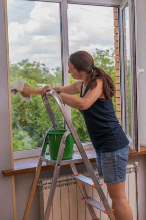 Back view of the young woman who washing the window with rag and window cleaner in the room. Cute...