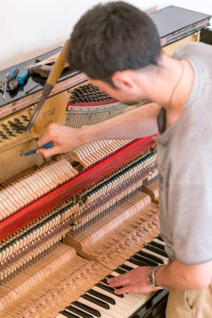 Piano tuning process. closeup of hand and tools of tuner working on grand piano. Detailed view of Upright Piano during a tuning. vertical photo. toned.の写真素材