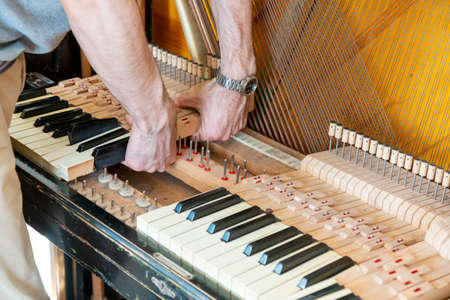 Piano tuning process. closeup of hand and tools of tuner working on grand piano. Detailed view of Upright Piano during a tuning. toned.の写真素材
