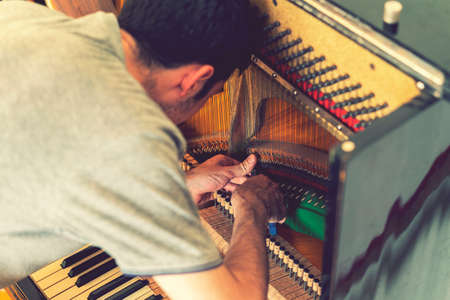 Piano tuning process. closeup of hand and tools of tuner working on grand piano. Detailed view of Upright Piano during a tuning. toned.の写真素材