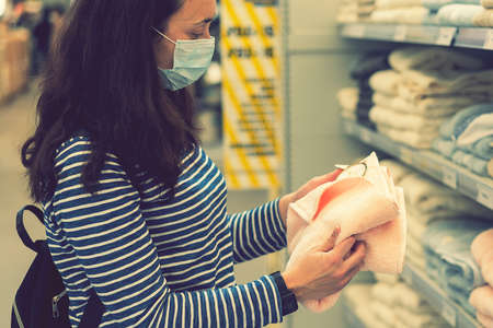 Woman in medical mask choosing goods in a store. Concept of shopping during quarantine pandemic. shopping at the time of the pandemic. Beautiful young women in a flu mask. tonedの写真素材