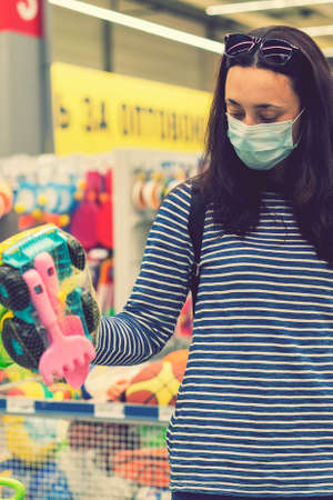 Woman in a protective mask in a supermarket chooses childrens toys. toned. vertical photo. tonedの写真素材