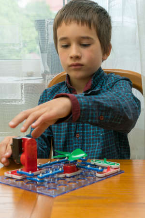 The boy playing an electric constructor. The child is played by intellectual toys. A boy in a blue shirt masters electronics. The concept of early development of children. vertical photoの写真素材