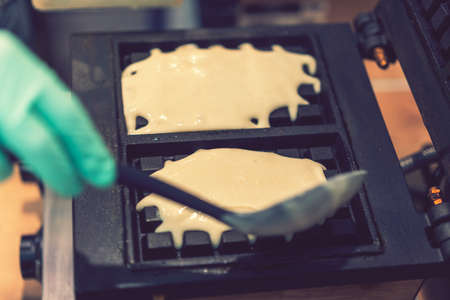 Waffle iron in the kitchen. Preparing homemade waffles, pouring a dough. Preparing of homemade waffles in twin waffle maker machine. Selective focus. tonedの写真素材