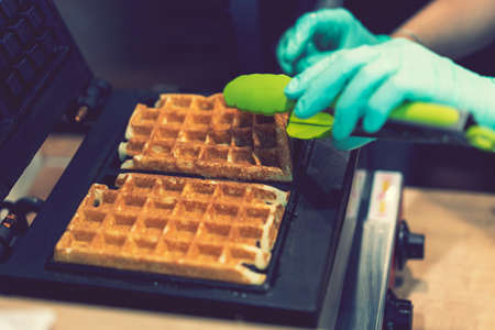 Waffle iron in the kitchen. Preparing homemade waffles, pouring a dough. Preparing of homemade waffles in twin waffle maker machine. Selective focus. tonedの写真素材