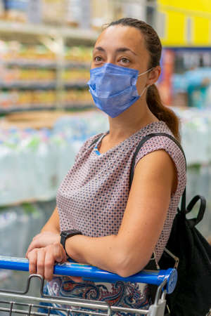 Alarmed female wears medical mask against virus while shopping in supermarket or store- health, safety and pandemic concept. Girl shopaholic in mall. vertical photo. toned. close upの写真素材