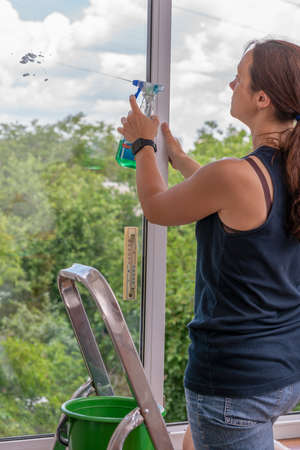 Back view of the young woman who washing the window with rag and window cleaner in the room. Cute girl with long hair washes a glass with detergent. toned. selected focus. tonedの写真素材