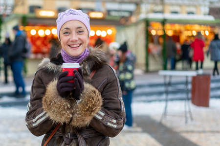 Beautiful young woman with coffee cup in the city. Beautiful woman with coffee on the street in winter clothes. Woman Having Hot Drink Outdoors On Winter Market. tonedの写真素材