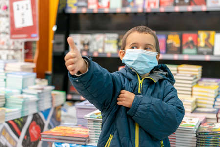 Boy in medical mask at bookstore. young boy chooses books in a bookshop. boy wear a protective mask In a bookstore. Concept of life And protect yourself from the virus outbreakの写真素材