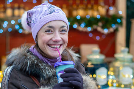 Beautiful young woman with coffee cup in the city. Beautiful woman with coffee on the street in winter clothes. Woman Having Hot Drink Outdoors On Winter Market.の写真素材