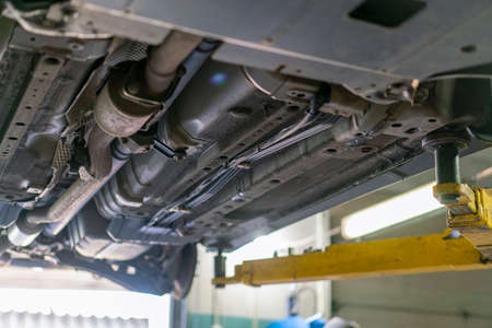 Car lifted in automobile service for fixing, worker repairs detail, telephoto. Car maintenance shop. Lifted chassis car for repairing under the car in garage shopの写真素材