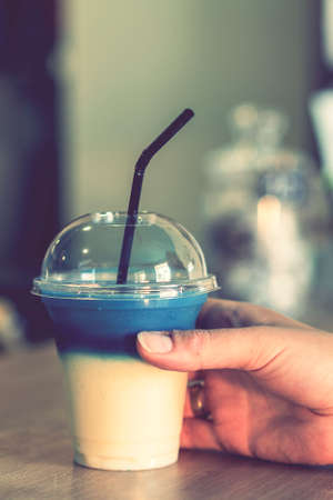Close up of womans hand hold cocktail in hand. Woman in restaurant. Womans hand holding a glass with blue colored drink. vertical photo. tonedの写真素材