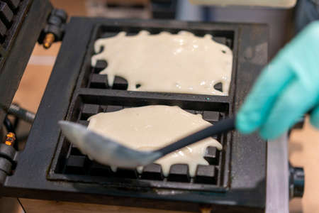 Waffle iron in the kitchen. Preparing homemade waffles, pouring a dough. Preparing of homemade waffles in twin waffle maker machine. Selective focusの写真素材