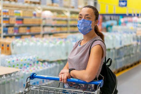 Alarmed female wears medical mask against coronavirus while shopping in supermarket or store- health, safety and pandemic concept. Girl shopaholic in mall. vertical photo. tonedの写真素材