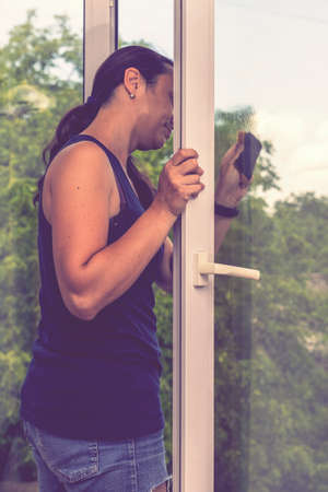 Back view of the young woman who washing the window with rag and window cleaner in the room. Cute girl with long hair washes a glass with detergent. toned. selected focus. tonedの写真素材
