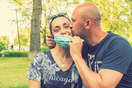 Photo of a young and attractive couple kissing in the park while wearing reusable face masks. End of virus pandemic, quarantine. virus crisis is over. tonedの写真素材