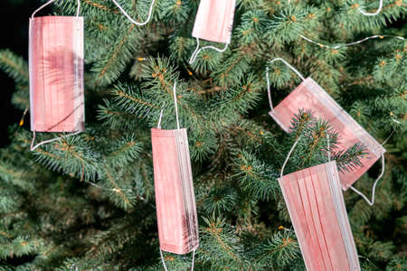Horizontal color image with a front view of a Christmas tree decorated with pink masks. Celebrating...