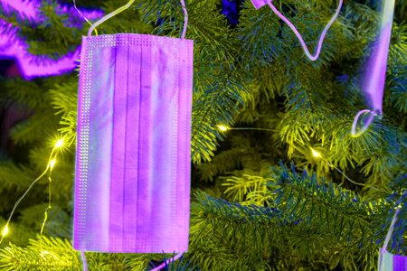 Horizontal color image with a front view of a Christmas tree decorated with pink coronavirus masks. Celebrating new 2021 year during  pandemic. tonedの写真素材