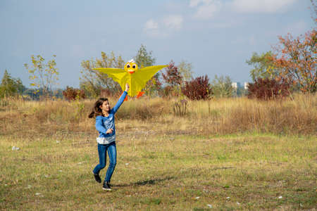 Teenage girl flying a yellow kite. Beautiful young girl kite fly. Happy little girl running with kite in hands on the beautiful field. vertical photo. tonedの写真素材