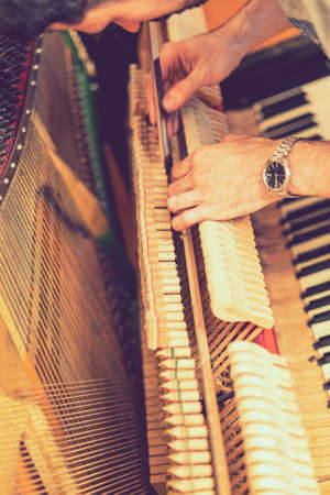 Piano tuning process. closeup of hand and tools of tuner working on grand piano. Detailed view of Upright Piano during a tuning. toned. toned. vertical photo. tonedの写真素材