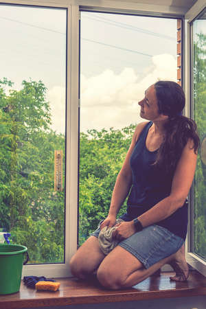 Attractive Woman Washing the Window. Cleaning Company worker working. Beautiful young woman is using a rag while cleaning windows. tonedの写真素材