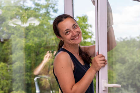 Smiling girl polishing the glass with cloth. Attractive Woman Washing the Window. Cleaning Company worker working. Beautiful young woman is using a rag while cleaning windowsの写真素材