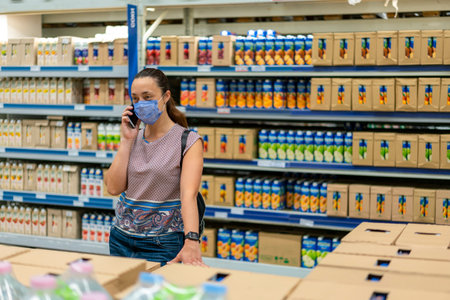 Woman wearing face mask and shopping in grocery store. Concept of protection against coronavirus and communication. Adult woman in medical mask using smartphone and shopping for groceriesの写真素材