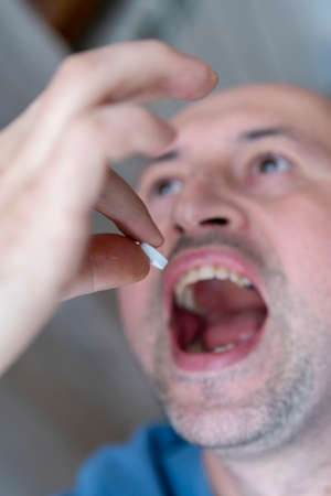 Extreme closeup man face taking white pill, mouth view swallowing pills, illness. man take medicine,open mouth and bring medicine to mouth. bluryの写真素材