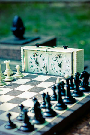 Chess board with pieces and clock on wooden desk In connection with the chess tournament. Chess pieces and stopwatch on a board in the park. tonedの写真素材