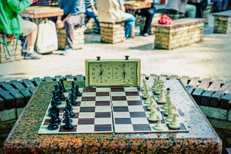 Chess board with pieces and clock on wooden desk In connection with the chess tournament. Chess pieces and stopwatch on a board in the park. tonedの写真素材