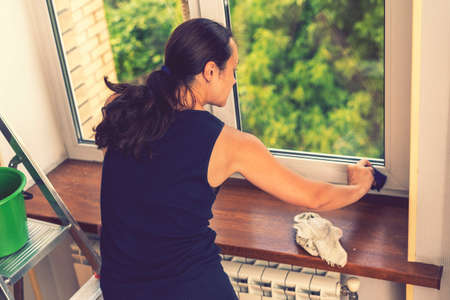 Attractive Woman Washing the Window. Cleaning Company worker working. Young woman washing window, close up. Cute girl with collected hair washes a glass with detergent. selected focus. tonedの写真素材