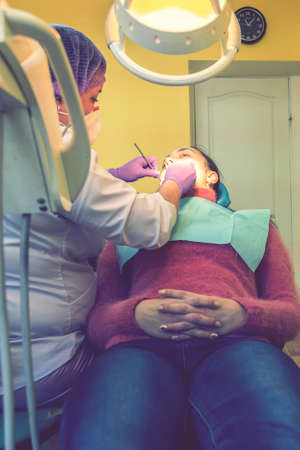 Male dentists examining and working on young female patient.Dentists office. Real woman in a chair at the dentist. vertical photo. tonedの写真素材