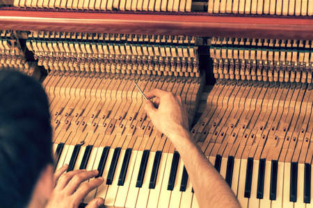 Piano tuning process. closeup of hand and tools of tuner working on grand piano. Detailed view of Upright Piano during a tuning. toned.の写真素材