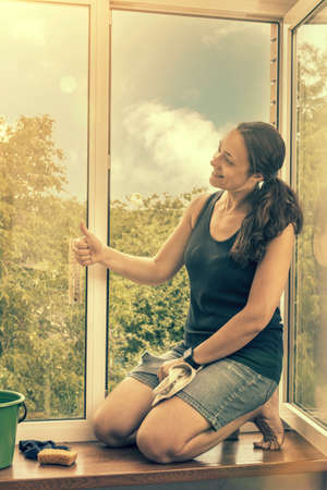 Beautiful woman cleaning window at home. A girl washes windows at home. To clean up the house. Long-haired woman cleaning windows with spray in home. toned.の写真素材