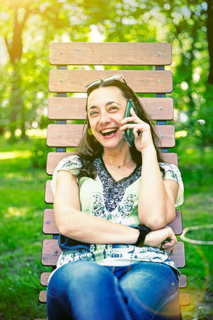 Young beautiful smiling woman talking on cell phone. Beautiful young female sitting on a park bench and talking on the phone. beautiful woman sitting on the park bench. tonedの写真素材