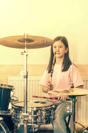 Happy girl in music therapy by playing drum kit on music room. Beautiful young girl drummer with drumsticks playing drums and cymbals. Female drummer. toned.の写真素材