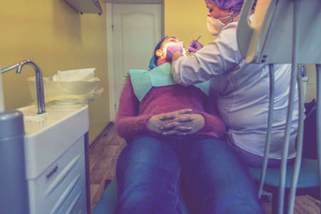 Male dentists examining and working on young female patient. Real woman in a chair at the dentist. toned.の写真素材
