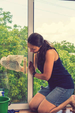 Beautiful woman cleaning window at home. A girl washes windows at home. To clean up the house. Long-haired woman cleaning windows with spray in home. toned.の写真素材