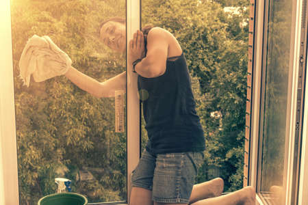 Beautiful woman cleaning window at home. A girl washes windows at home. To clean up the house. Long-haired woman cleaning windows with spray in home. toned.の写真素材
