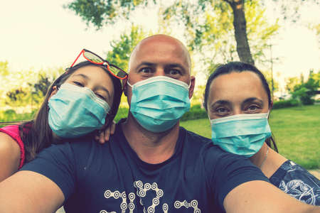 Family in protective medical masks. Mother, father, daughter protect themselves from the virus Coronavirus. Family in medical masks outdoors. close up. tonedの写真素材