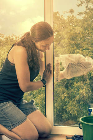 Beautiful woman cleaning window at home. A girl washes windows at home. To clean up the house. Long-haired woman cleaning windows with spray in home. tonedの写真素材