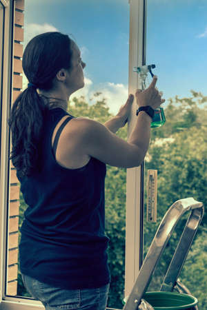 Beautiful woman cleaning window at home. A girl washes windows at home. To clean up the house. Long-haired woman cleaning windows with spray in home. tonedの写真素材