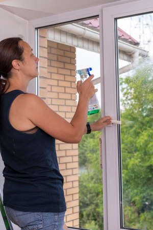 Beautiful woman cleaning window at home. A girl washes windows at home. To clean up the house. Long-haired woman cleaning windows with spray in home. tonedの写真素材